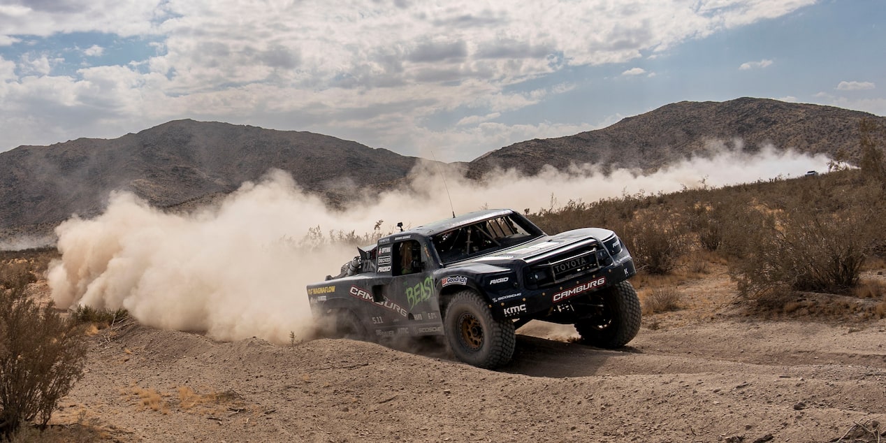 Three Quarters View of a Black Vehicle Speeding through the Desert Leaving behind Dust Clouds