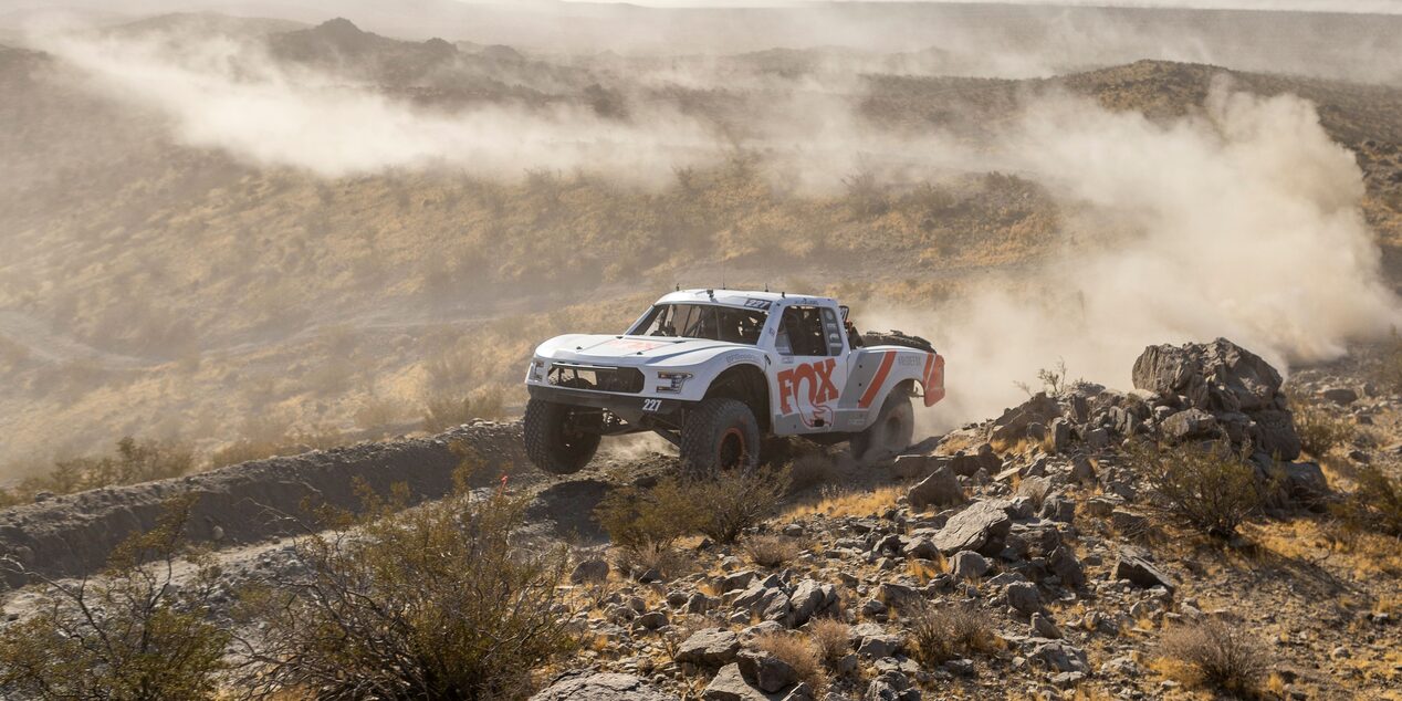 Three Quarters View of a White Custom Vehicle Racing Down a Rocky Road in a Desert