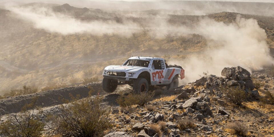 Three Quarters View of a White Custom Vehicle Racing Down a Rocky Road in a Desert
