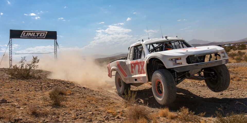Front View of a Custom White Vehicle on the Side of the Frame Racing in a Desert Leaving behind Dust