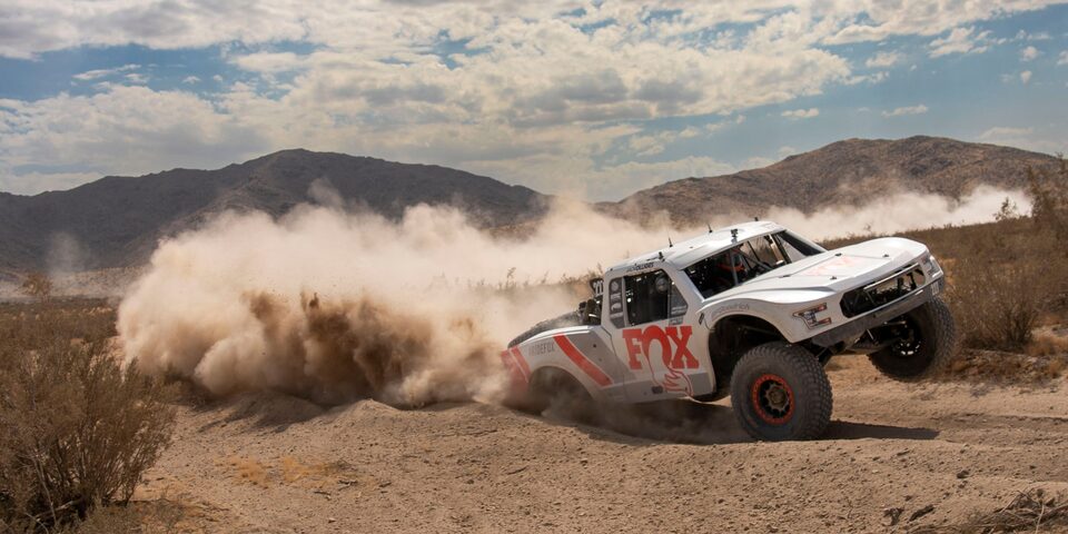 Three Quarters View of a White Custom Vehicle Racing Down a Rocky Road in a Desert
