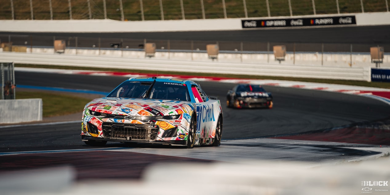 Three Quarters View of a Custom Chevy Racecar Driving Down the Track with Sunlight Hitting Its Front