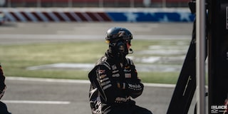 A Racer Is Seen Sitting Down with a Black Outfit on While Looking In the Distance