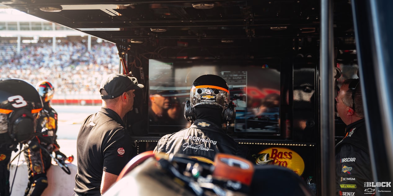 Rear View of a Racer Wearing a Helmet Watching the Race Along with Other Team Members