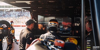 Rear View of a Racer Wearing a Helmet Watching the Race Along with Other Team Members