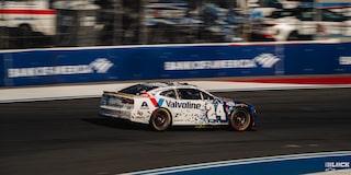 Three Quarters Rear View of a White Chevy Racecar Driving Down the Track in the Afternoon