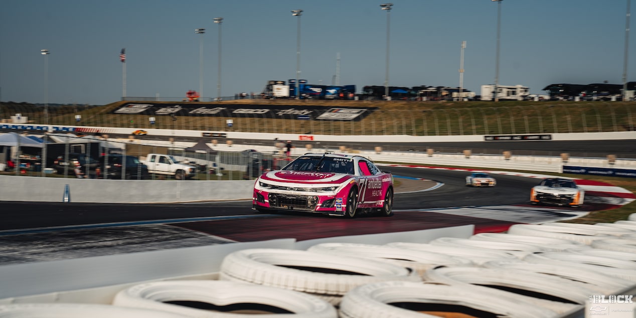 Three Quarters View of Racecars Driving Down the Track with White Tires Lined up Next to It