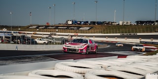 Three Quarters View of Racecars Driving Down the Track with White Tires Lined up Next to It