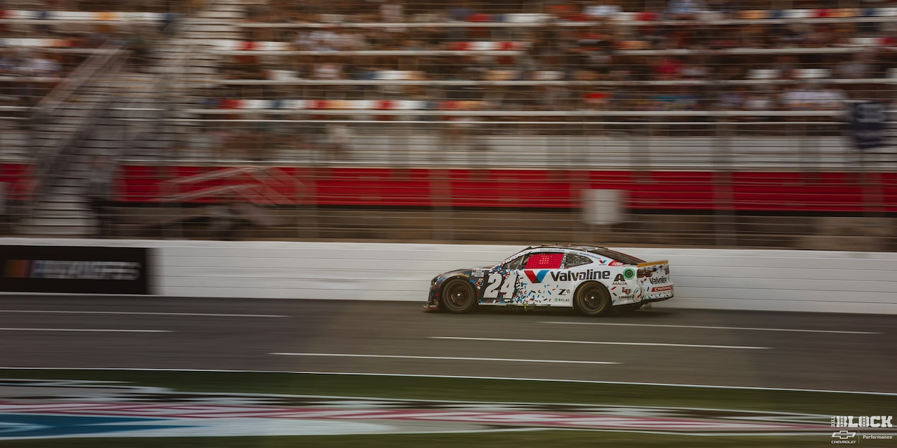 Three Quarters Rear View of a Custom Racecar Driving Down the Track in Front of a Crowded Stadium