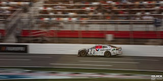 Three Quarters Rear View of a Custom Racecar Driving Down the Track in Front of a Crowded Stadium