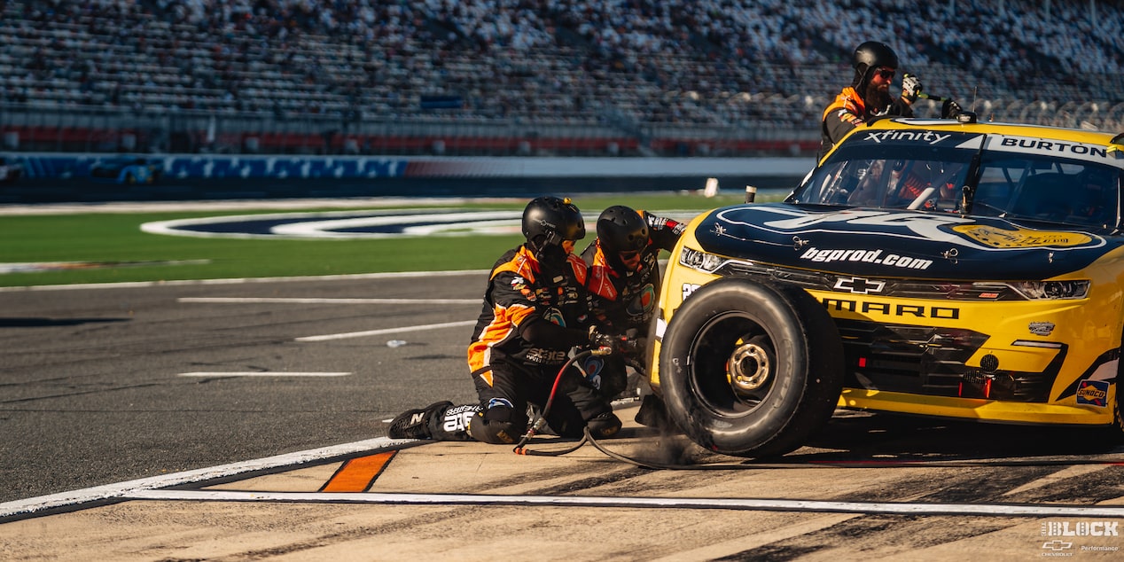 A Yellow Racecar Is Parked on the Side of the Track with Three Support Staff Changing Its Tires