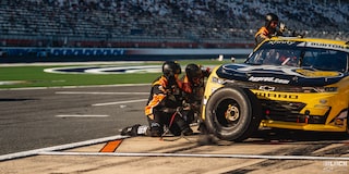 A Yellow Racecar Is Parked on the Side of the Track with Three Support Staff Changing Its Tires