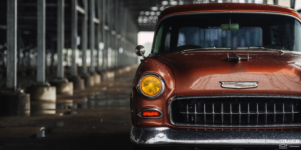 Front View of a Wet Chevy 1955 Handyman Wagon on the Left Side of the Frame under the Shade in Rainy Weather