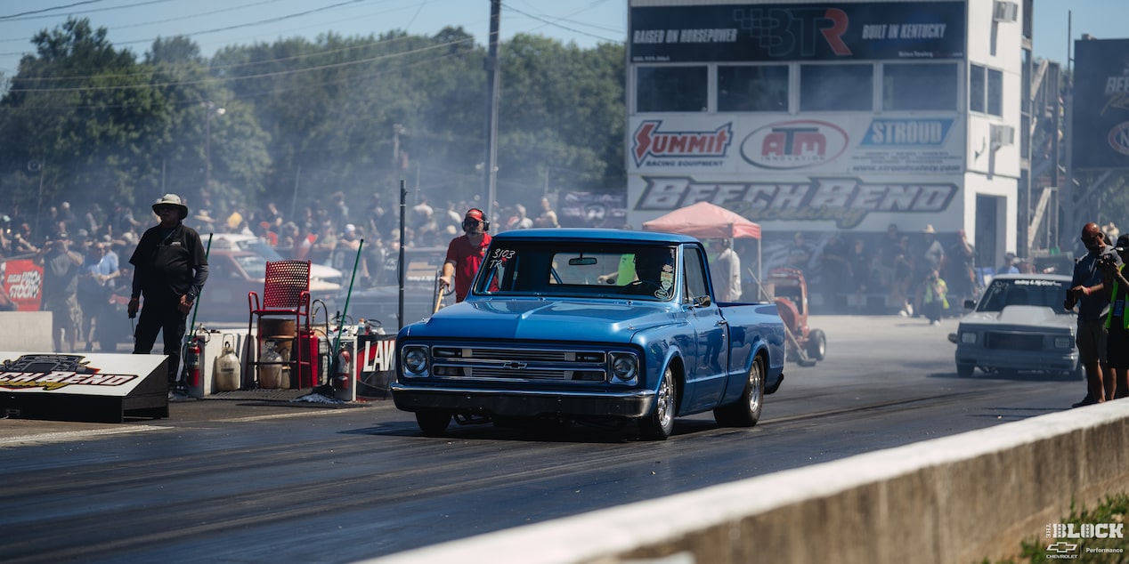 Three Quarters View of a Blue 1967 Chevy C10 Truck on the Road with  People and Smoke Behind It