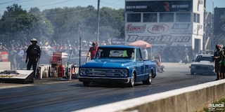 Three Quarters View of a Blue 1967 Chevy C10 Truck on the Road with  People and Smoke Behind It